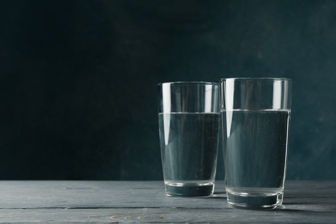 Two glasses of water in dark room on marble table, copy space