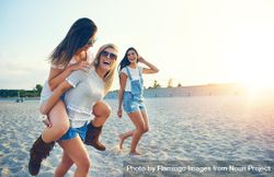 Three happy female friends having fun walking on sand at the beach 5rQdZ0