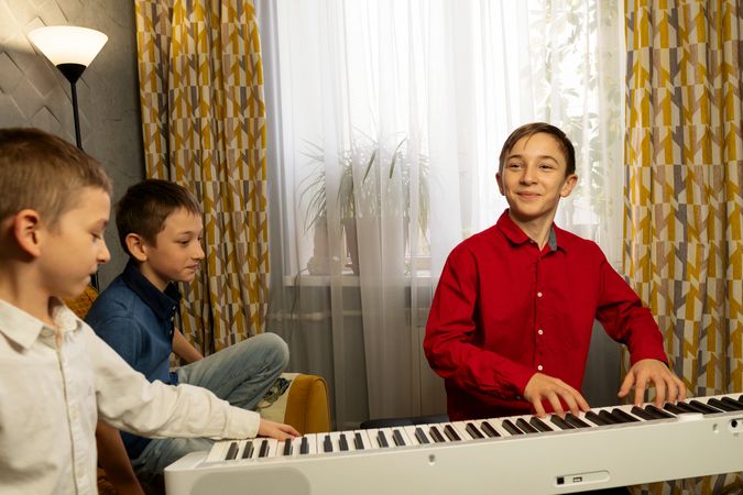 Boy smiling while playing the piano as friends watch.