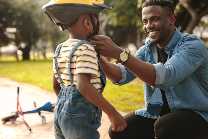Smiling man helping son wearing helmet for cycling at park
