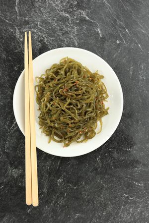 Plate of green shirataki noodles served with chopsticks