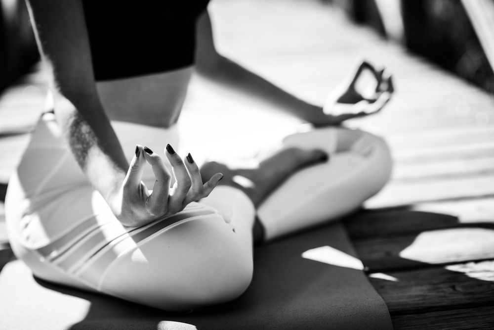 Close up of woman wearing sport clothes meditating on yoga mat on forest path, monochrome