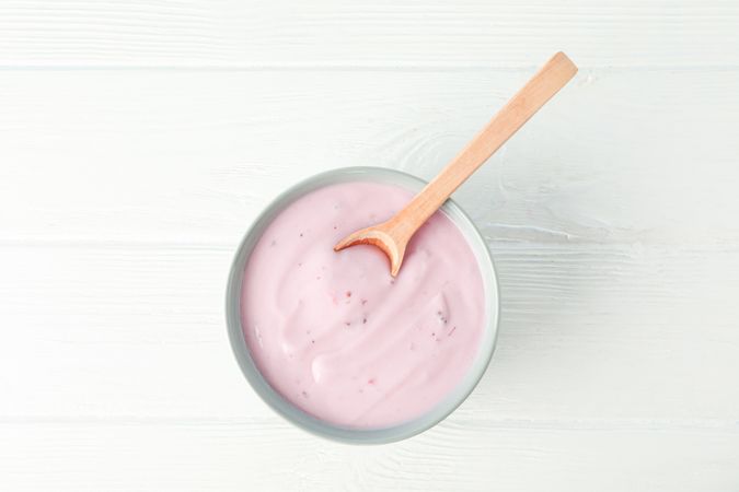 Fruit yogurt in bowl and spoon on wooden background