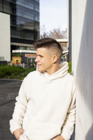 Portrait of young male in bright hoodie leaning on wall outside