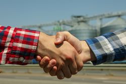 Businessmen shake hands against silos. Agriculture business
