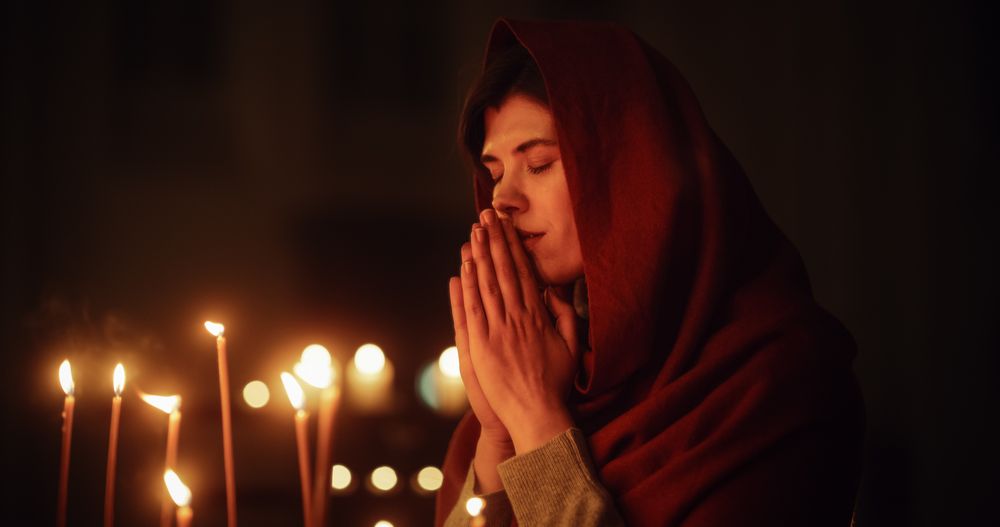Christian Woman Getting on her Knees and Praying Near the Candles in a Church.