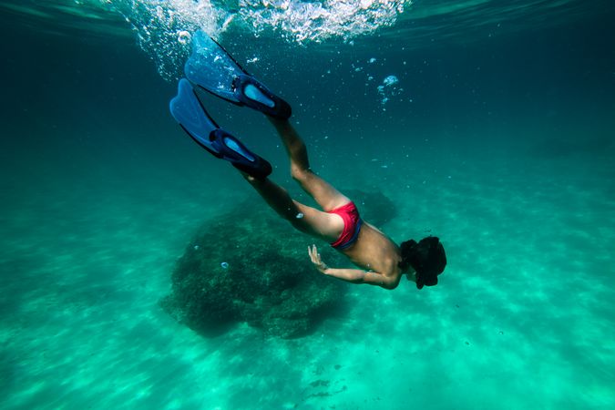 Teenager snorkeling in diving mask and fins observing sea bottom
