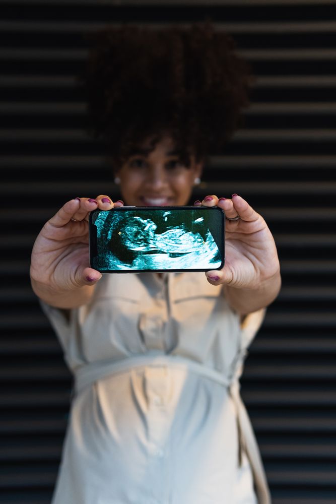 Smiling Black woman showing smartphone screen with baby ultrasound