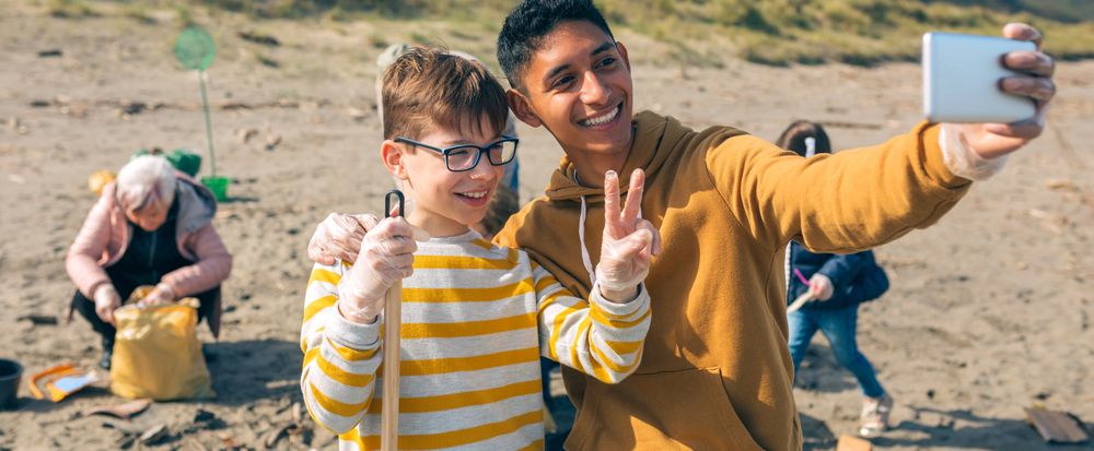 Young man and boy taking selfie to group of volunteers cleaning beach