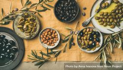 Olives in bowls with branches, on beige table linen, with serving spoon, wide composition 0P68O4