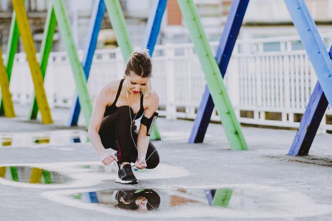 Woman with earphones lacing shoes on street