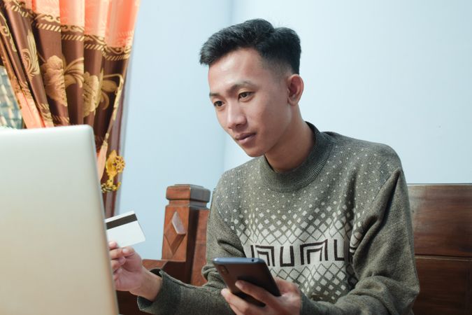 Asian man in sweater shopping online holding credit card and smartphone