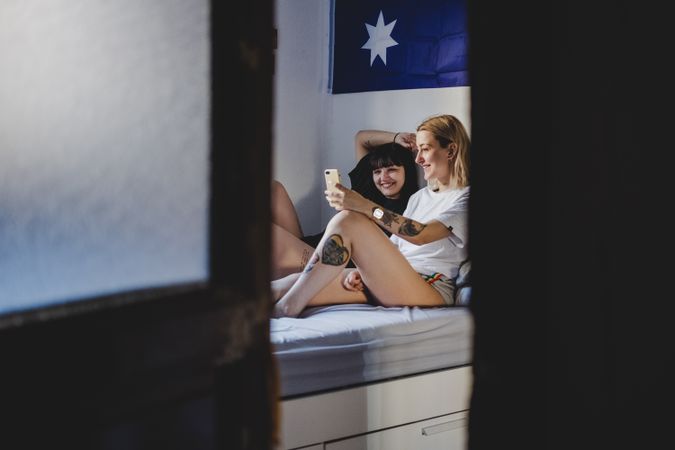 Happy lesbian couple using smartphone on bed