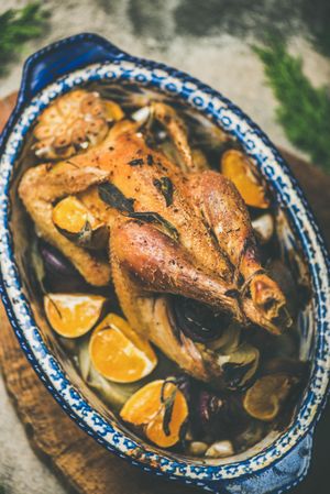 Close up of roast chicken with oranges in decorative roasting dish