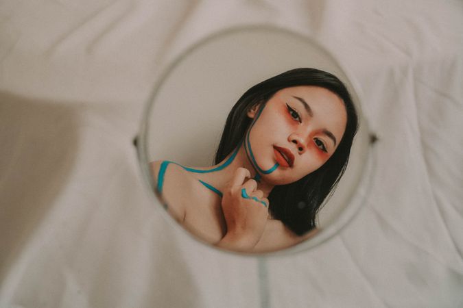Reflection of woman drawing on herself with blue marker on round mirror