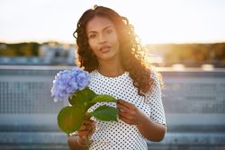 Black woman holding leaf on blue flower