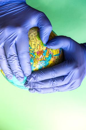 Hands in blue latex gloves holding globe, with copy space