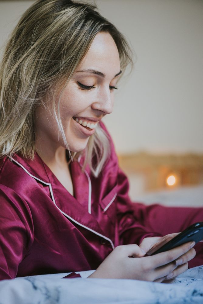 Woman lying down on bed with smartphone