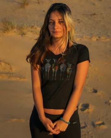Portrait of young woman in dark shirt and pants standing on brown sand