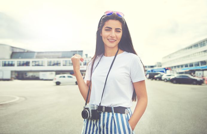 Relaxed brunette woman with hand in pocket and camera around neck
