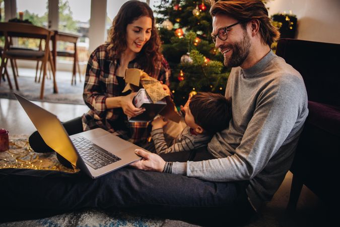 Man having video call on his laptop with his son and wife opening Christmas gifts