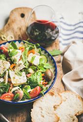 Greek salad with feta, tomatoes, and red wine on wooden board, vertical composition, selective focus