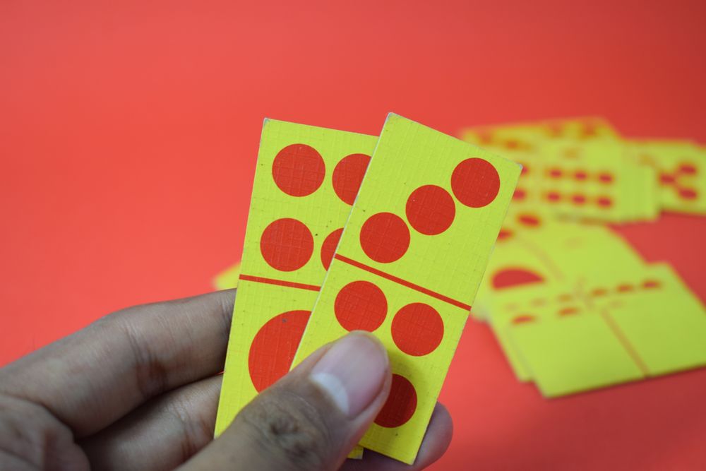 Person holding domino cards over red table
