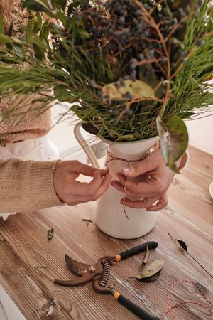Faceless florist working with bunch of twigs arranged in vase