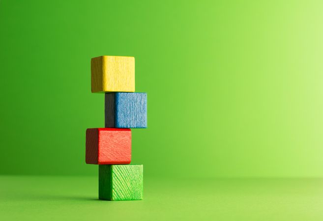 Colorful wooden blocks stacked  to the left of frame over green background