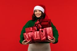 Woman in Santa hat holding stack of red Christmas presents.