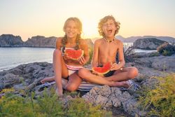 Laughing brother and sister enjoying watermelon on seashore