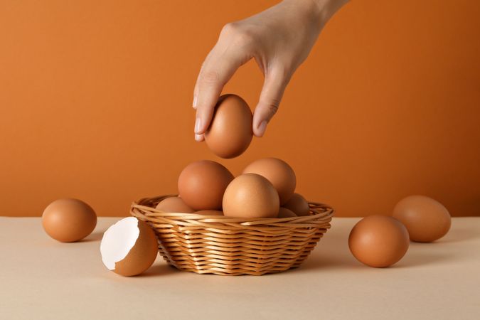 Eggs in a wicker basket, with a hand, on an orange background.