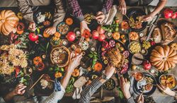 Group of people serving food and pouring wine at festive table with roast chicken, squash and pie