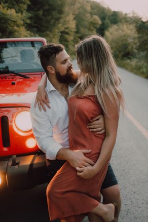 Loving couple sitting on car on road near forest