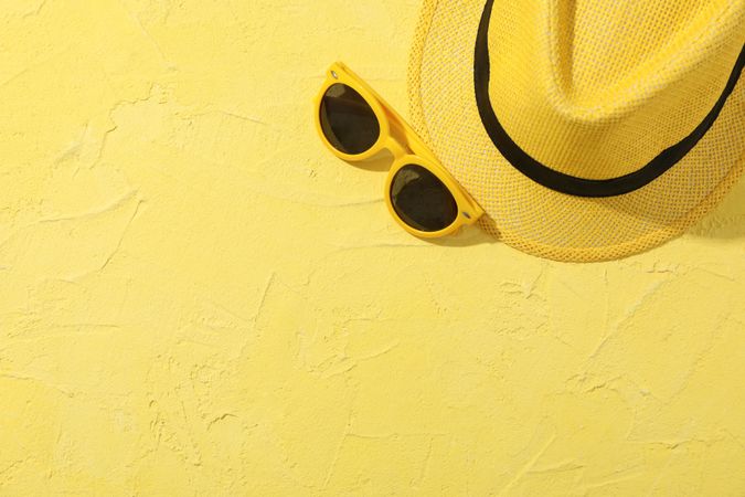 Hat and sunglasses on yellow background, top view