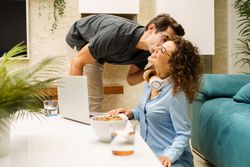 Happy couple with laptop having fun while working remotely in living room