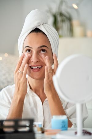 Young woman with towel on head applying skin care cream