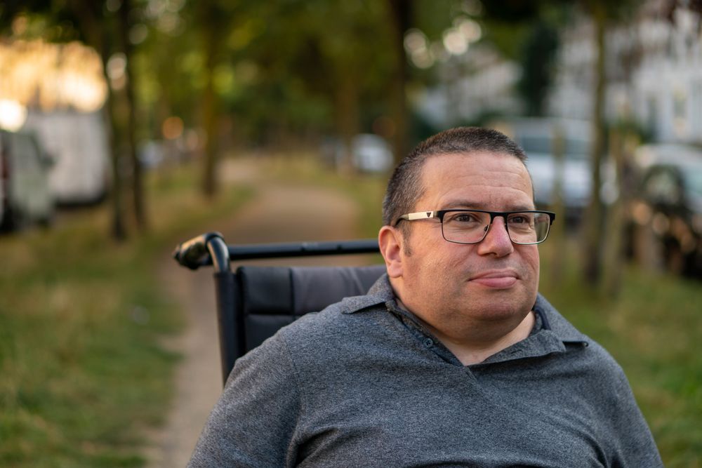Portrait of content man sitting in wheelchair in park path