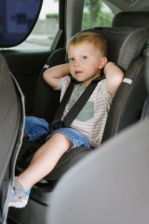 Kid boy sitting on backseat with seat belts in car during daytime