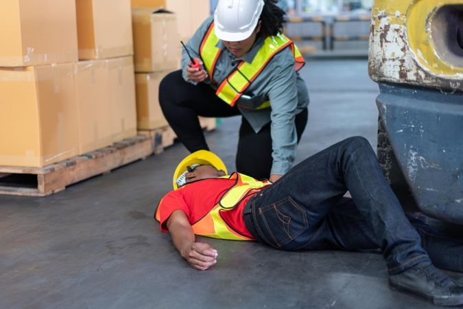 Black male in PPE gear passed out on warehouse floor with colleague offering help
