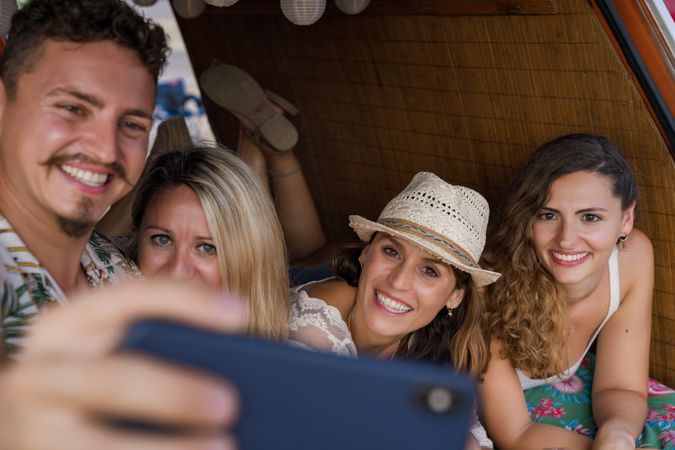 Smiling man taking selfie with girlfriends comfortable placing on trunk of blue car