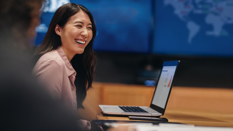 Smiling young woman sitting at table with laptop in meeting room