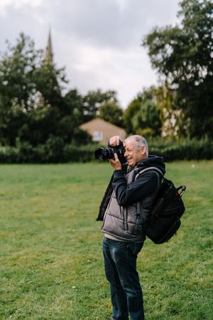 Older man taking a picture in a field, vertical