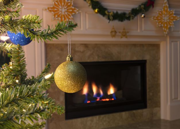 Golden ornament on tree with glowing fireplace in background