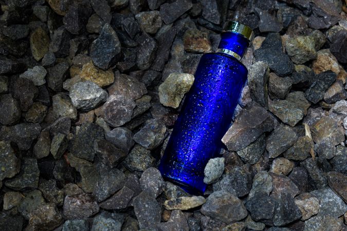 Wet blue perfume bottle mock up laying in rocky terrain