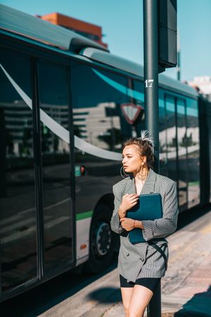 Woman with tablet in stylish suit standing nearby bus