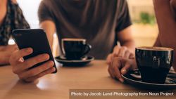 Close up of a smartphone being used by a man sitting at a cafe table with his friends 4jnZ84