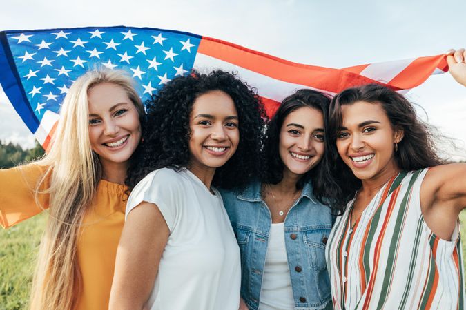 Female friends posing with American flag above their head
