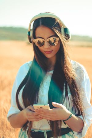 Woman wearing sunglasses holding smartphone and listening to music