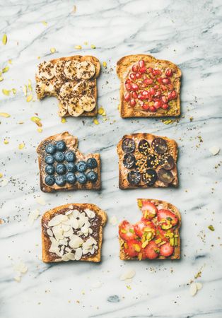 Slices of toasts with bites taken out, with different fresh fruit toppings on marble counter